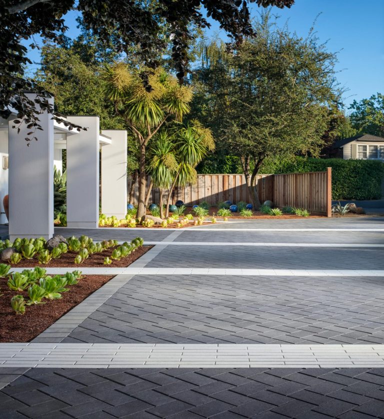 Modern driveway featuring gray and white pavers, surrounded by lush landscaping and palm trees, showcasing quality brick paving services by Molinason Brick Pavers in Jupiter, FL.