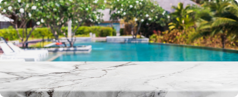 Marble surface in foreground with blurred pool and lush greenery in background, illustrating luxury outdoor living space for pool decks.