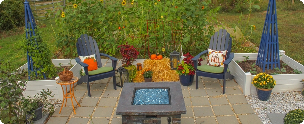 Outdoor patio and raised garden beds at sunset, decorated for Autumn with pumpkins, plants, hay bales, chrysanthemum and lanterns