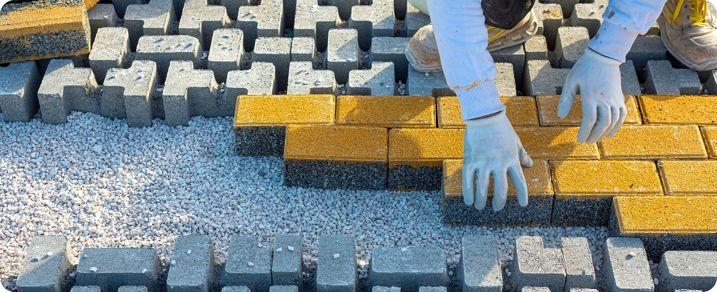 Paving stone worker is putting down pavers during a construction of a city street onto sheet nonwoven bedding sand and fitting them into place.