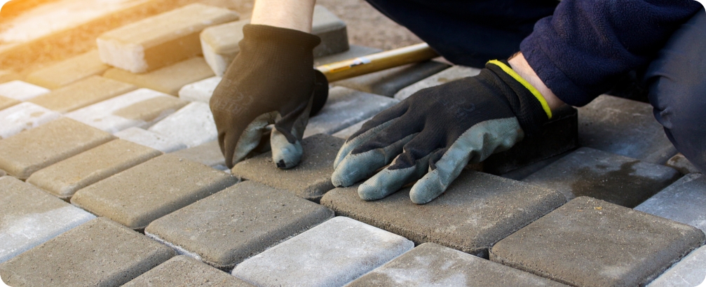 Defocus paver master. Man lays paving stones in layers. Garden brick pathway paving by professional worker. Hands of worker installing concrete paver blocks by rubber hammer. Out of focus.
